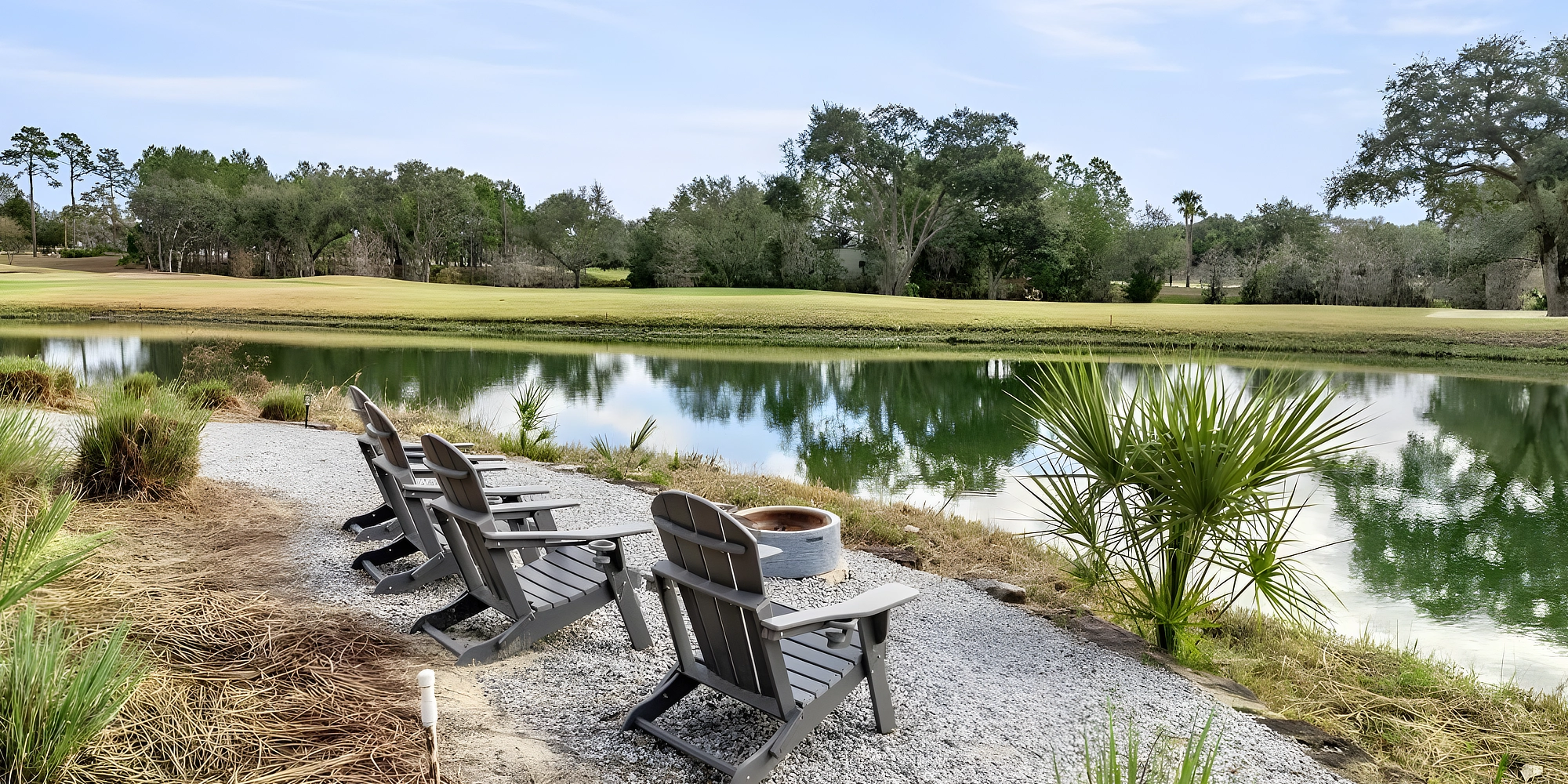 Adirondack chairs around a fire pit at the edge of the pond, with the golf course behind