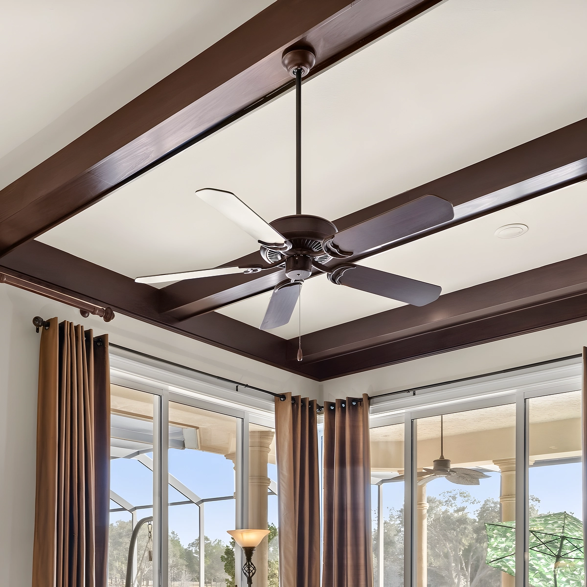 Dark wood ceiling beams and a ceiling fan over the family room windows