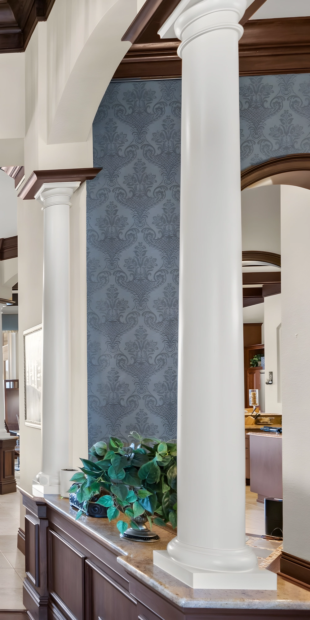 A white column on a wood half-wall in the foyer, with an arched doorway and a damask wall behind it