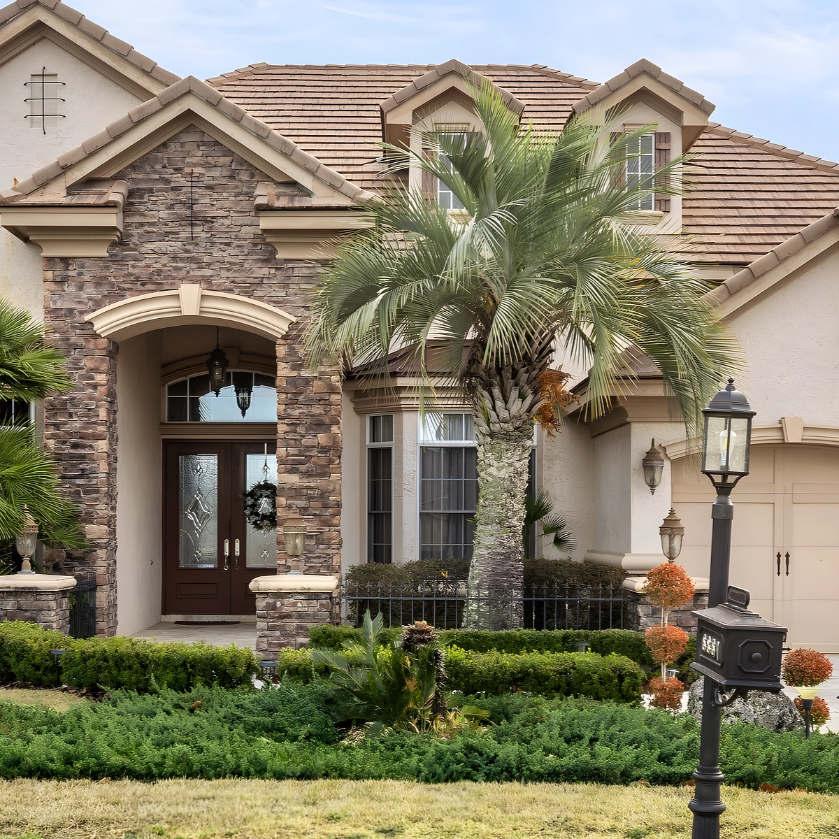 The stone entry arch and front door under the tile roof, with palms and hedges