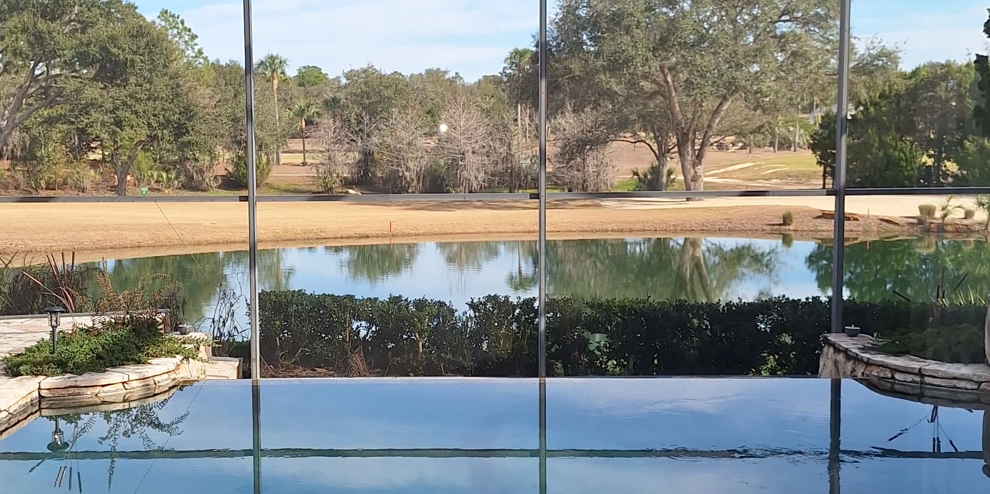 The pool's infinity edge seen from the deck, with the pond and the golf course beyond the screen