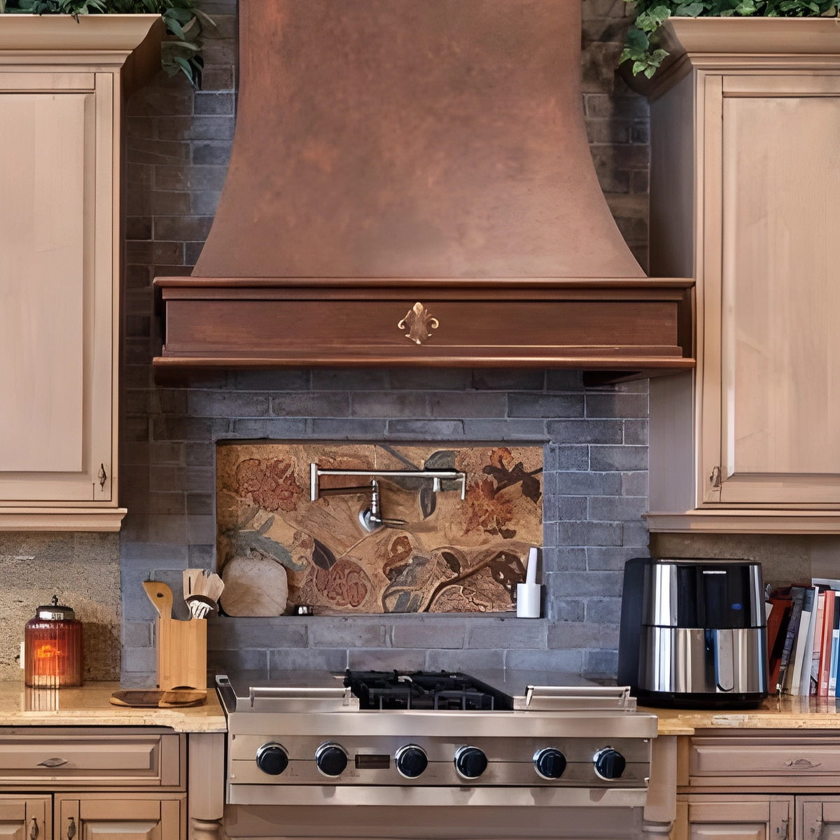 Copper range hood over a stainless gas range, with a pot filler set into a tile mural