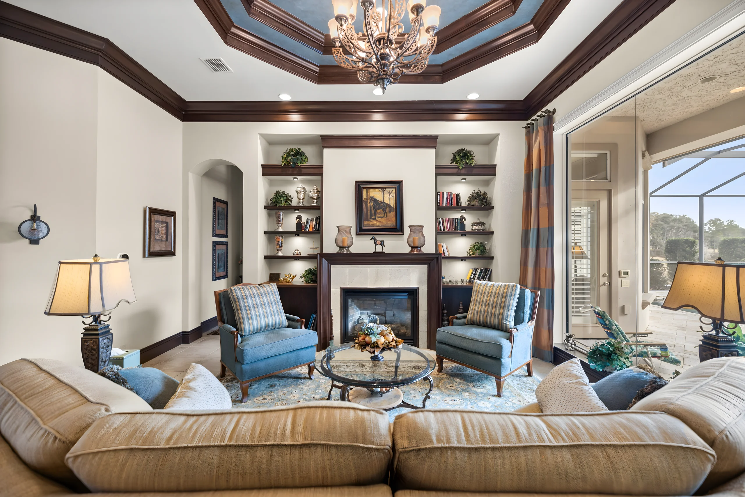 Formal living room with a blue tray ceiling, the fireplace between built-in shelves, and sliders to the lanai