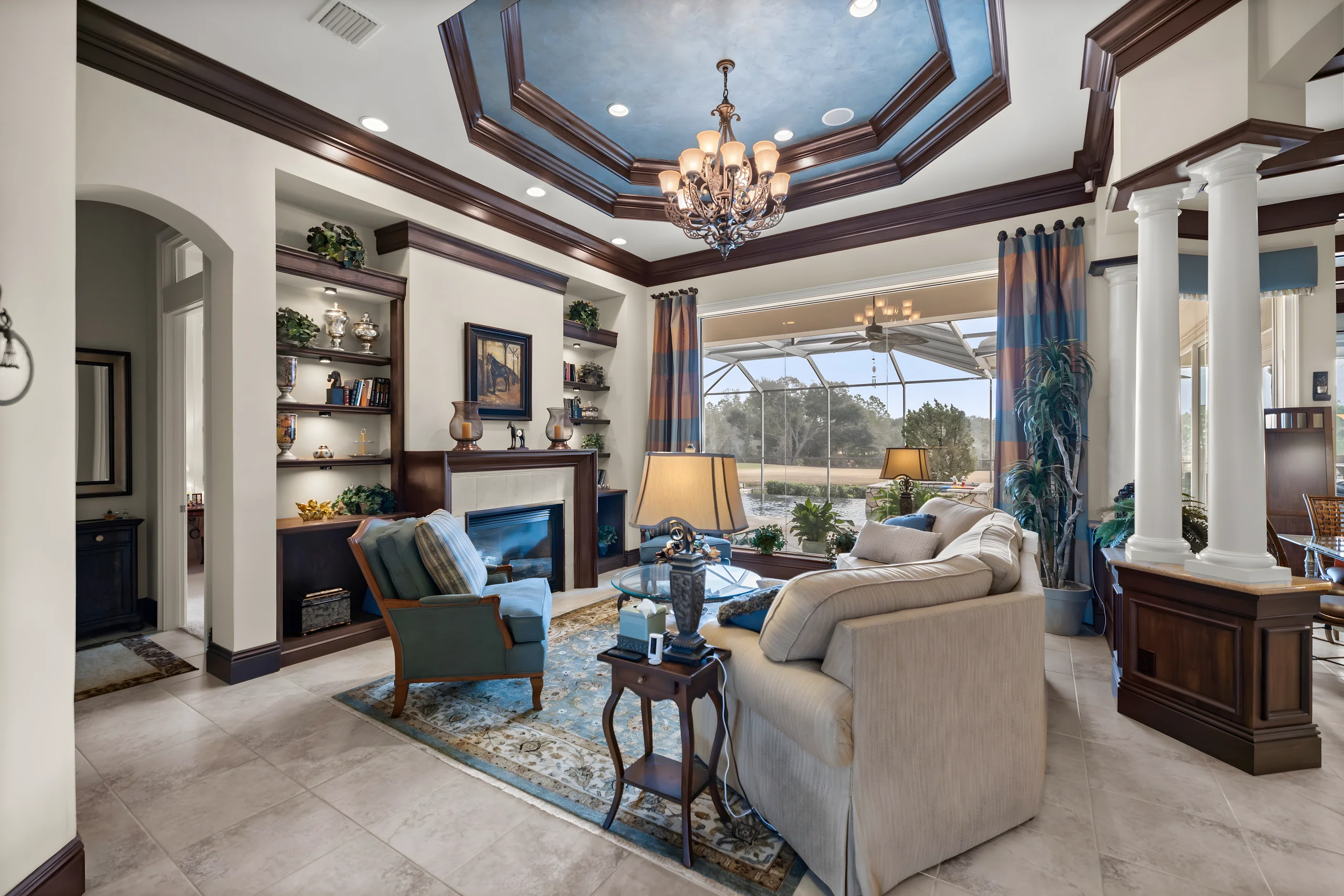 Formal living room with columns and the fireplace, and a view through the lanai to the pond