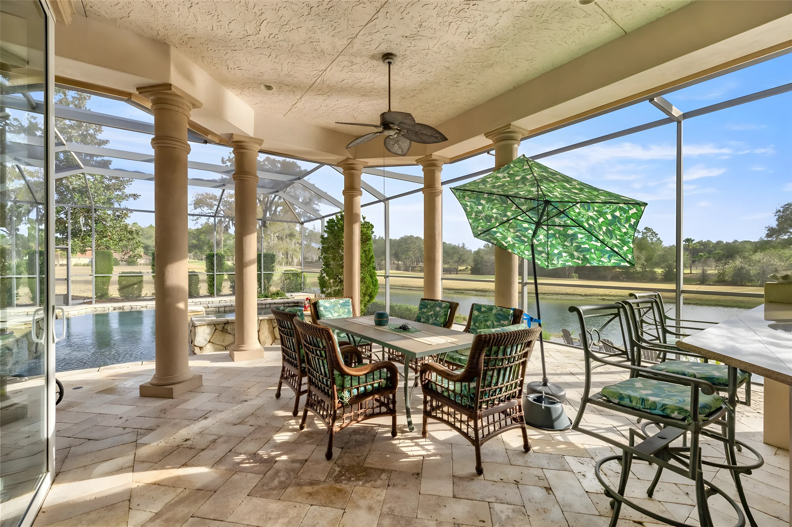 Covered lanai with columns and the dining area, the pool and the pond beyond the screen