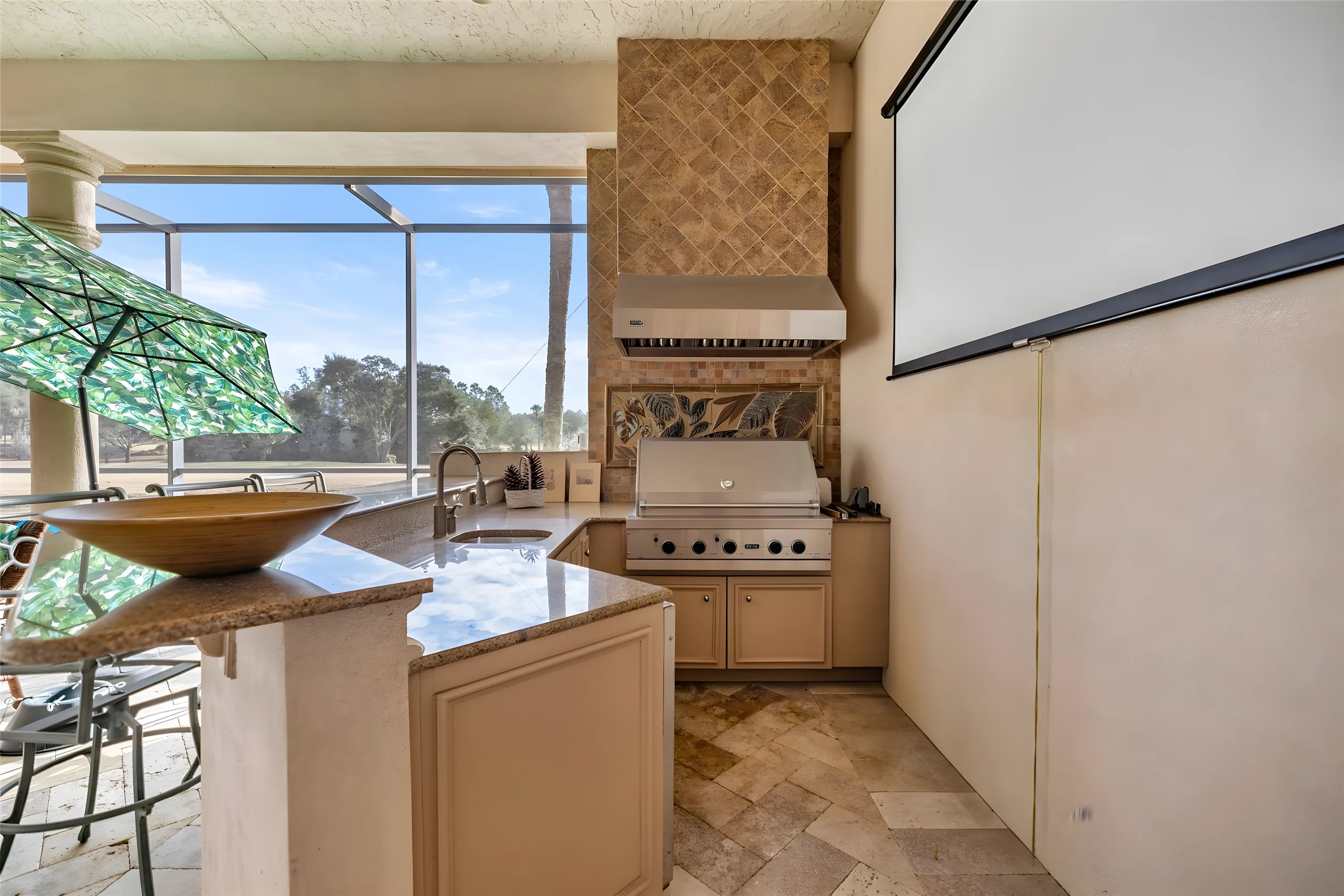 Outdoor kitchen on the covered lanai with a built-in grill, range hood, sink and granite counter