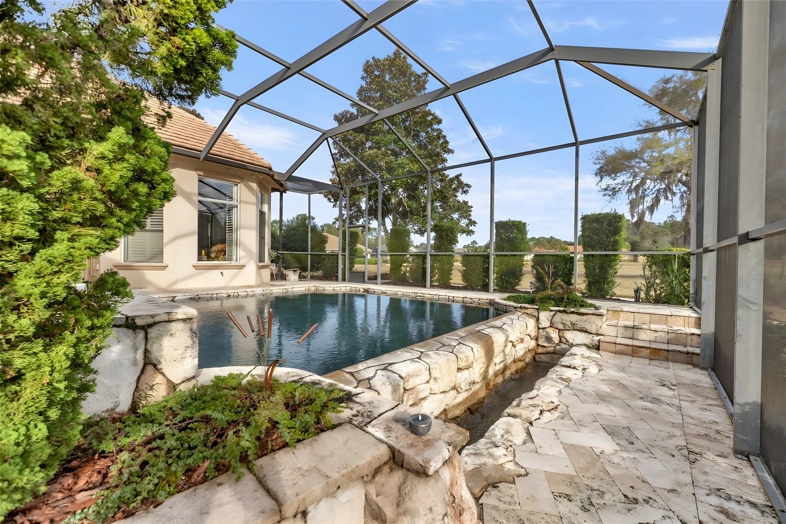 The infinity edge spilling into a stone catch basin, with planting along the screen enclosure