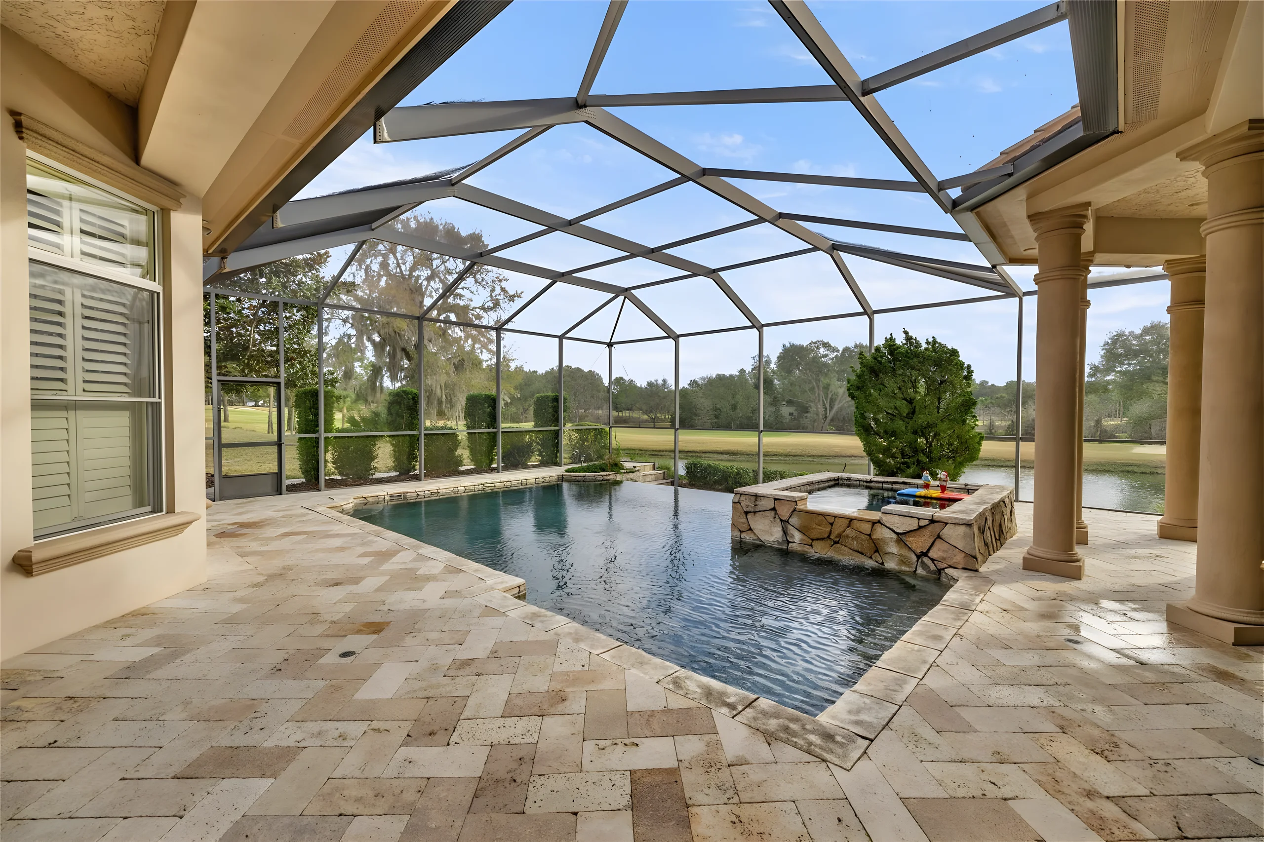 Pool and raised stone spa seen from the covered lanai, with the pond and the golf course beyond