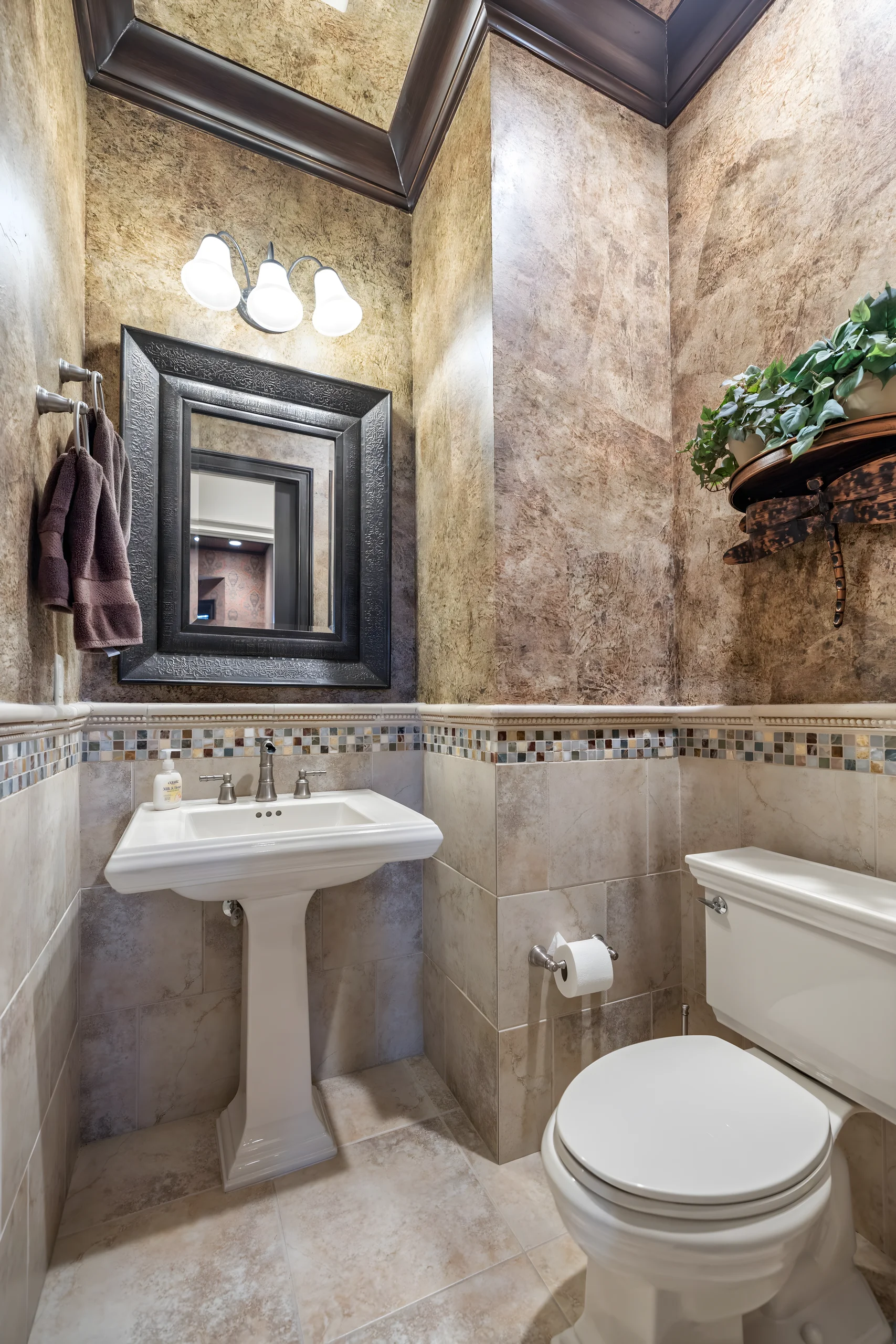 Office bathroom with a pedestal sink, travertine walls and a framed mirror