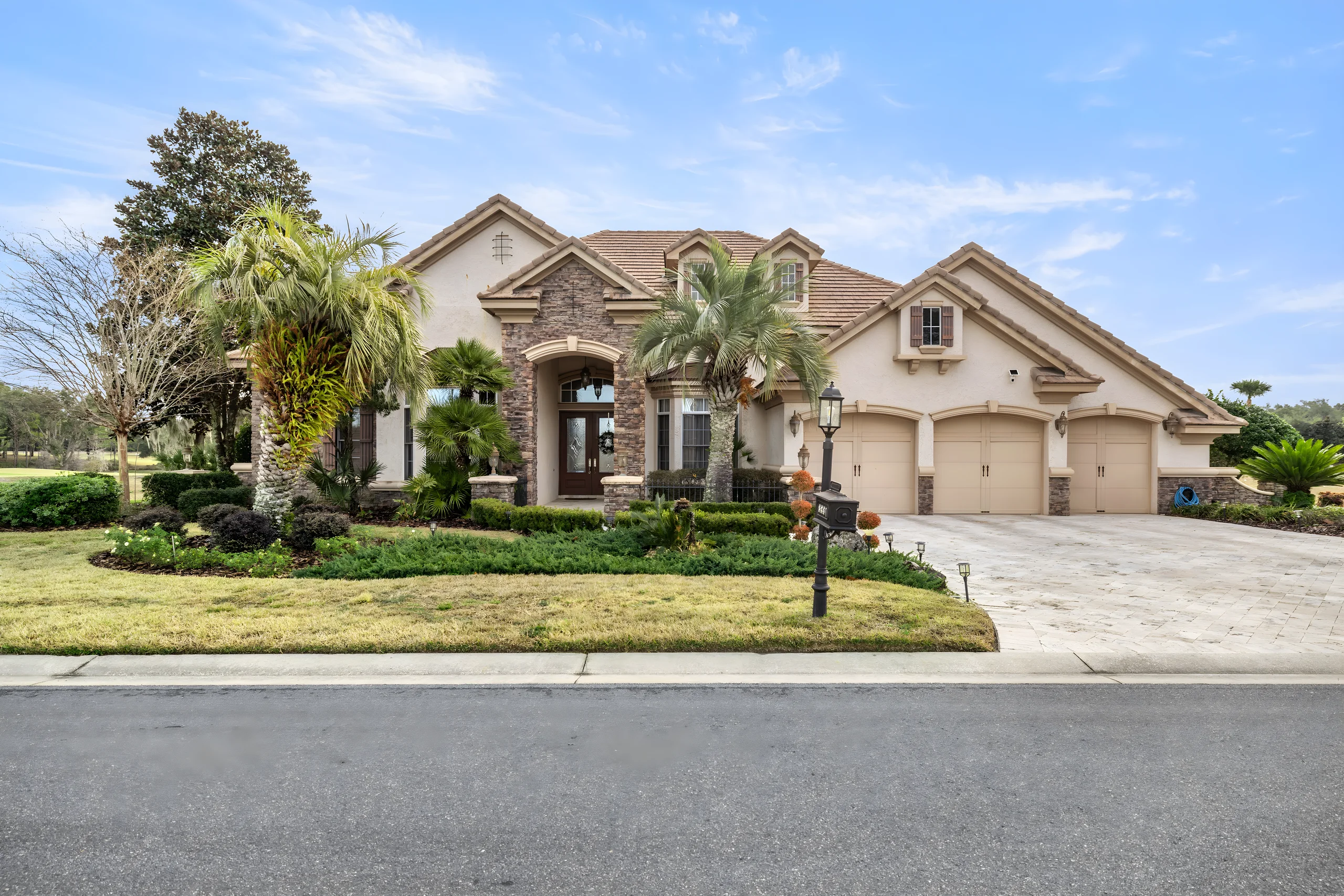 Front of the house from the street: stone and stucco, a tile roof, palms and a three-car garage